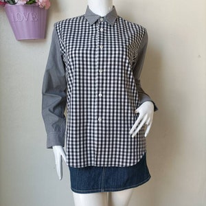 May include: A black and white checkered long-sleeve shirt with a button-up front and a collar. The shirt is on a white mannequin and is paired with a denim skirt.