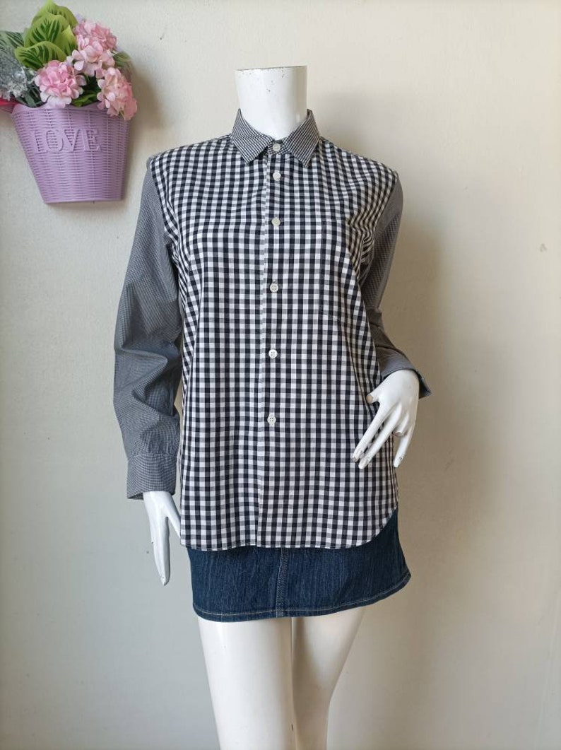 May include: A black and white checkered long-sleeve shirt with a button-up front and a collar. The shirt is on a white mannequin and is paired with a denim skirt.