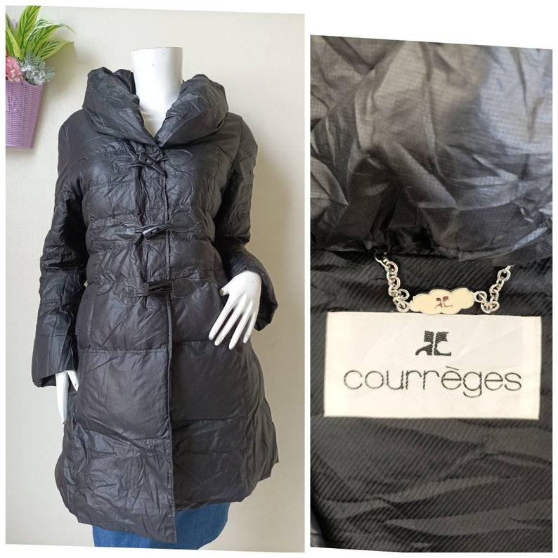 May include: A dark grey, quilted coat with a large collar and toggle fastenings. The coat is displayed on a mannequin. The Courr&egrave;ges label is visible in a close-up shot. The coat has a long, streamlined silhouette.