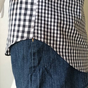 May include: A black and white gingham shirt tucked into a pair of blue denim jeans.