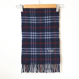 May include: A blue and red plaid scarf with fringe. The scarf has a small black label that says "Burberry's" in white letters.