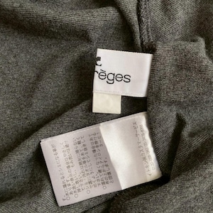 Puede incluir: Primer plano de una tela gris oscuro con dos etiquetas blancas. Una etiqueta tiene el nombre de la marca "r&egrave;ges" impreso. La otra etiqueta contiene texto japon&eacute;s con instrucciones de cuidado. La tela parece ser un material de punto.