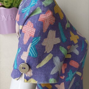 May include: Purple dress with a colorful abstract print. The dress has short sleeves with a button on each cuff.