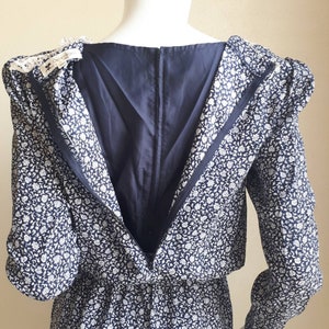 May include: A navy blue dress with a white floral print. The dress has a long sleeve and a zipper down the back. The dress is on a white mannequin.