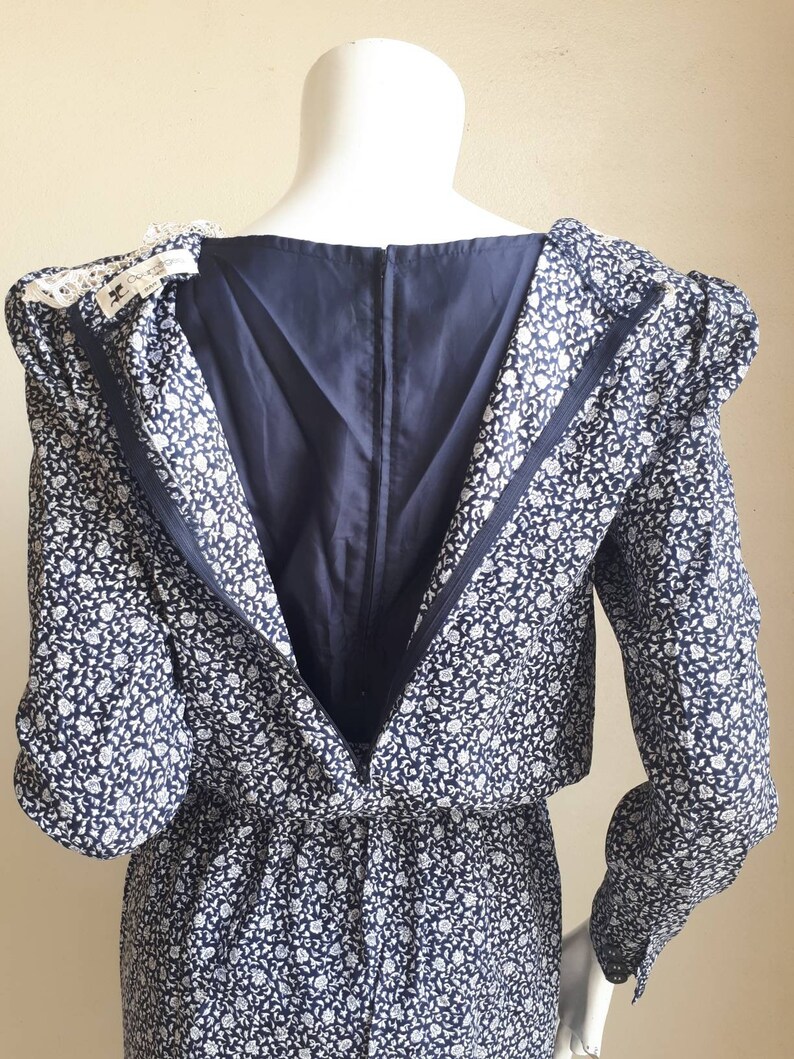 May include: A navy blue dress with a white floral print. The dress has a long sleeve and a zipper down the back. The dress is on a white mannequin.