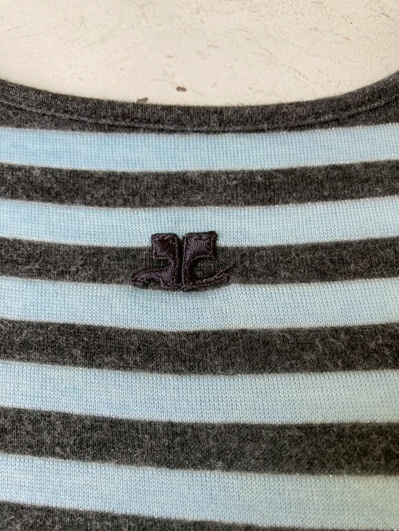 Puede incluir: Primer plano de una camiseta a rayas grises y celeste. La camiseta tiene un peque&ntilde;o logotipo bordado de dos botas. El cuello es redondo. La tela parece suave y c&oacute;moda.