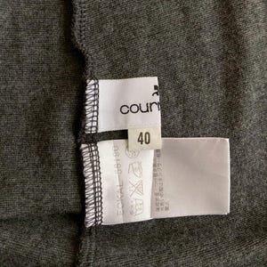 Puede incluir: Primer plano de una prenda gris oscuro con etiquetas blancas. Una etiqueta dice "count" y el n&uacute;mero "40". Otra etiqueta muestra s&iacute;mbolos de cuidado y texto. La tela tiene una apariencia texturizada.