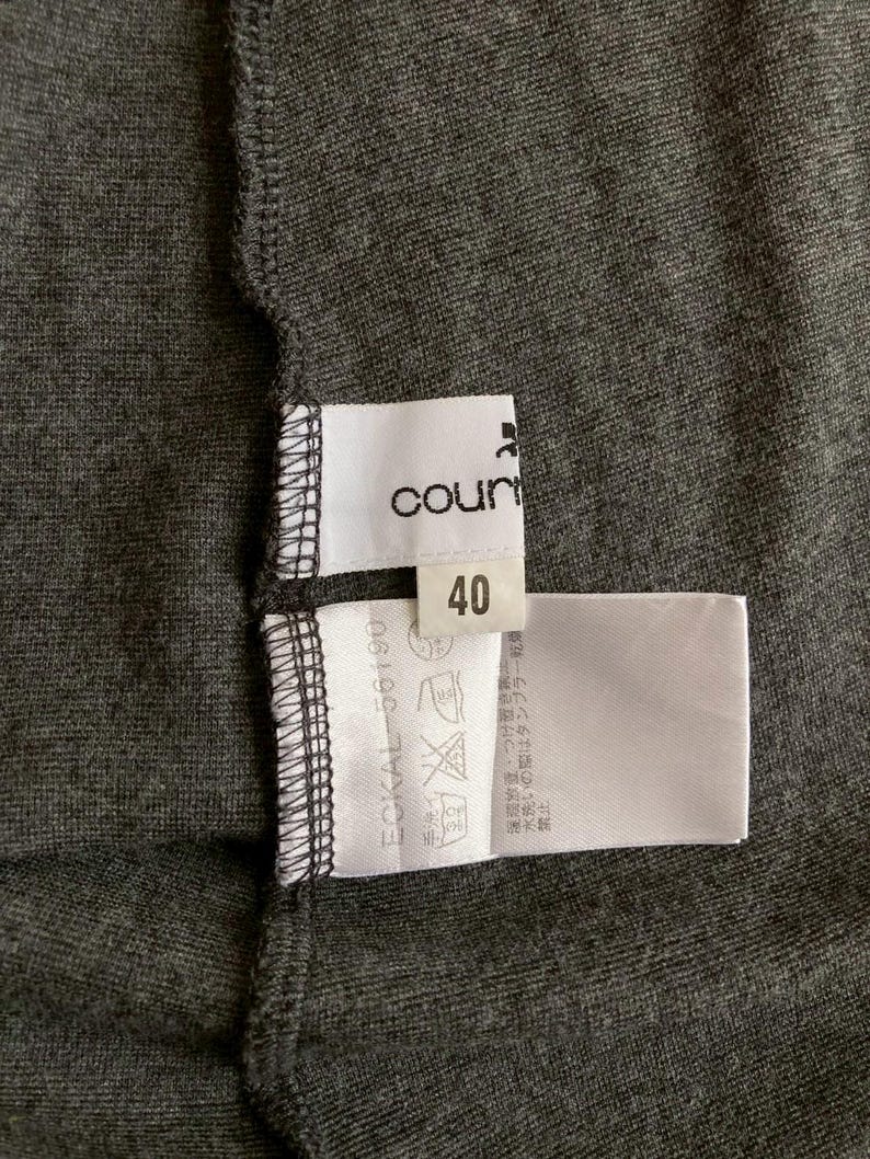 Puede incluir: Primer plano de una prenda gris oscuro con etiquetas blancas. Una etiqueta dice "count" y el n&uacute;mero "40". Otra etiqueta muestra s&iacute;mbolos de cuidado y texto. La tela tiene una apariencia texturizada.