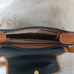 May include: A black leather shoulder bag with brown leather trim and a zipper closure. The bag is open and the inside is lined with a brown fabric.