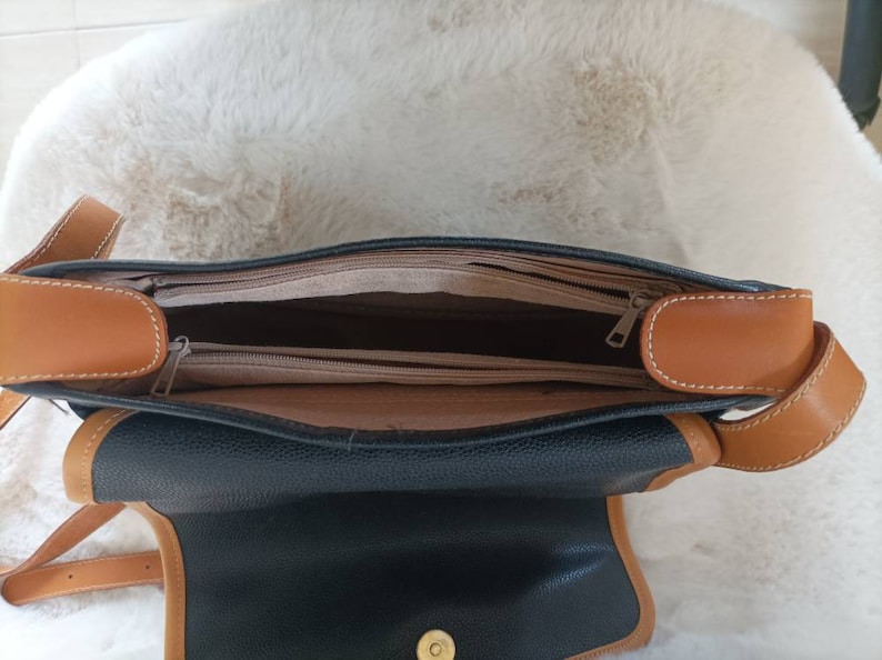 May include: A black leather shoulder bag with brown leather trim and a zipper closure. The bag is open and the inside is lined with a brown fabric.