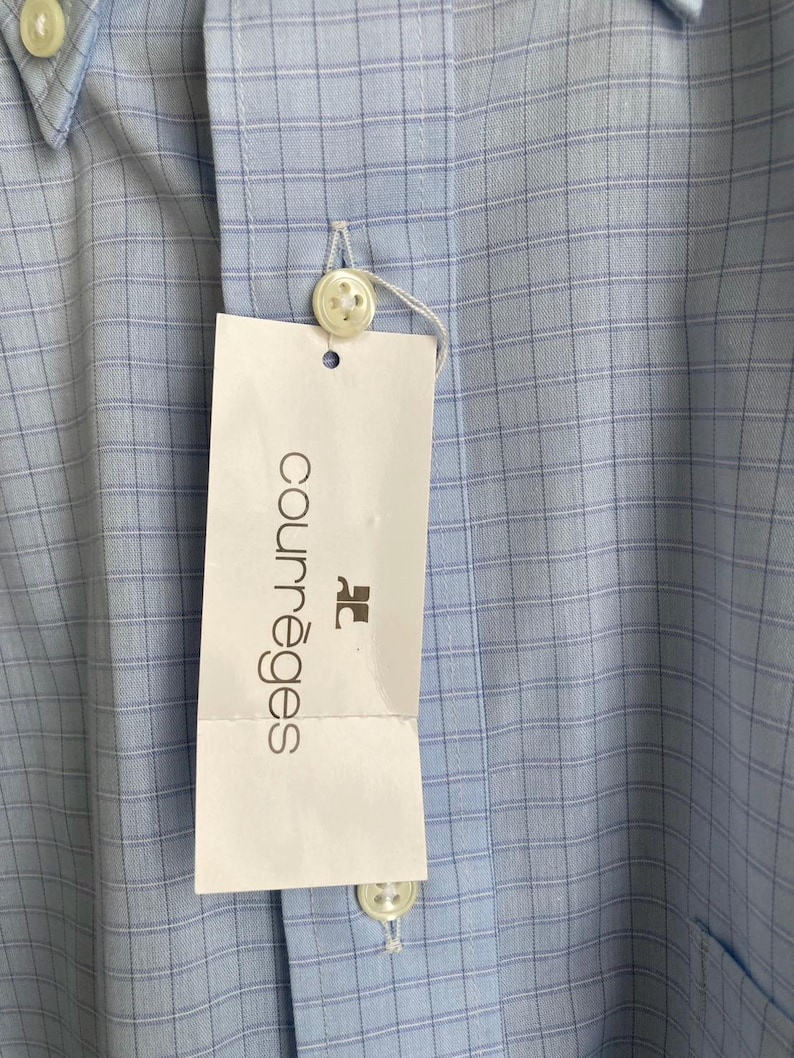 May include: A light blue button-down shirt with a white and light blue checkered pattern. The shirt has a white tag with the text "Courr&egrave;ges" in black.