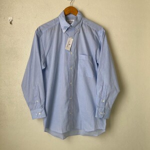 May include: A light blue long-sleeved button-down shirt with a white and light blue checkered pattern. The shirt has a single chest pocket and a white tag with the text "Original Penguin" on it.