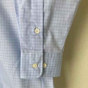 May include: A light blue dress shirt with a white and blue checkered pattern. The shirt has a button-down collar and long sleeves with button cuffs.