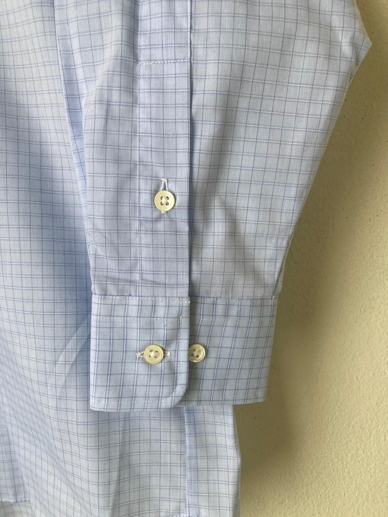 May include: A light blue dress shirt with a white and blue checkered pattern. The shirt has a button-down collar and long sleeves with button cuffs.