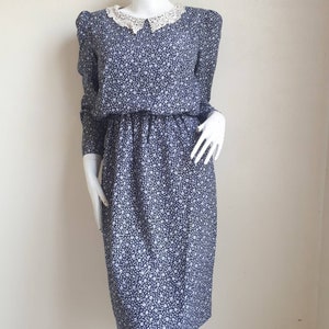 May include: A blue and white floral dress with a white lace collar. The dress has long sleeves and a fitted bodice.