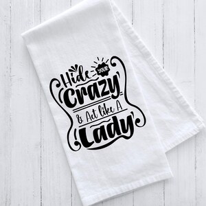 May include: White kitchen towel with black text that reads "Hide Your Crazy & Act Like A Lady".