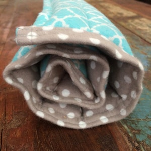 May include: Rolled-up, quilted fabric item with a light blue geometric pattern on the exterior. The interior and trim are a light brown color with white polka dots. The item is rolled up, showing the interior fabric.