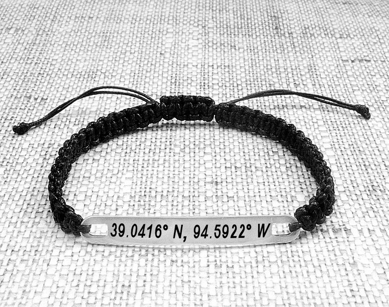 May include: Black braided bracelet with a silver tag engraved with the coordinates "39.0416&deg; N, 94.5922&deg; W".