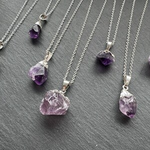 May include: Seven silver necklaces with amethyst crystal pendants. The crystals are various shapes and sizes, and some have a purple hue.