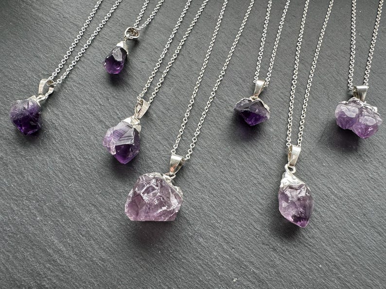 May include: Seven silver necklaces with amethyst crystal pendants. The crystals are various shapes and sizes, and some have a purple hue.