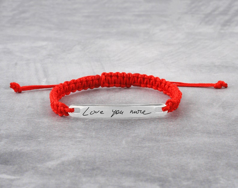May include: Red string bracelet with a silver bar charm engraved with the handwritten message "Love you more".