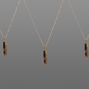 May include: Three gold necklaces with pendant crystals. Each necklace has a slender, gold chain suspending a vertical, rectangular crystal with brown and black tones. The crystals have a pointed bottom.