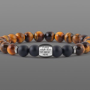May include: A brown and black tiger's eye beaded bracelet with black matte beads and a silver charm that says "PLACE YOUR TEXT OR IMAGE HERE".