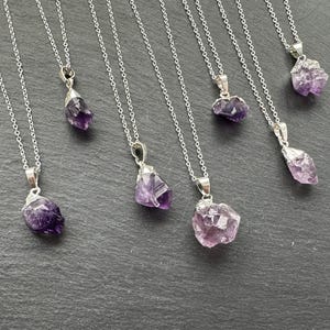 May include: Seven silver necklaces with amethyst crystal pendants. The amethyst crystals are all different shapes and sizes, and they have a purple and light purple color.
