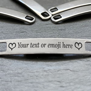 May include: A silver metal tag with two heart shapes and the text "Your text or emoji here".