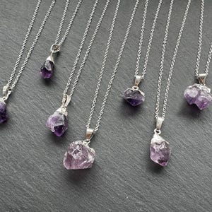 May include: Seven silver necklaces with amethyst crystal pendants. The crystals are various shapes and sizes, some are rough and some are polished.