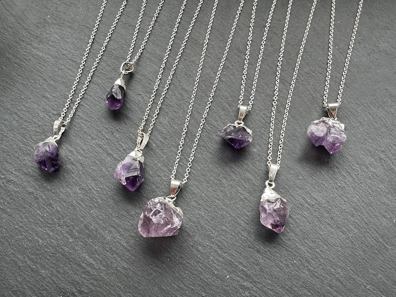 May include: Seven silver necklaces with amethyst crystal pendants. The crystals are various shapes and sizes, some are rough and some are polished.