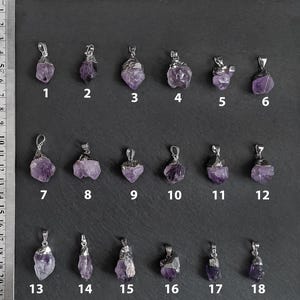 May include: Eighteen amethyst crystal pendants with silver settings. The pendants are arranged in three rows of six. Each pendant is numbered 1 through 18.