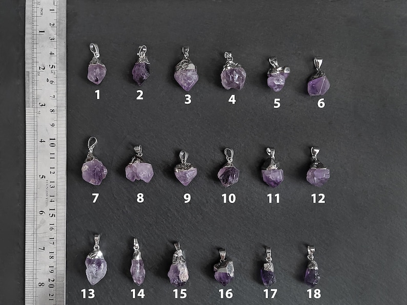 May include: Eighteen amethyst crystal pendants with silver settings. The pendants are arranged in three rows of six. Each pendant is numbered 1 through 18.