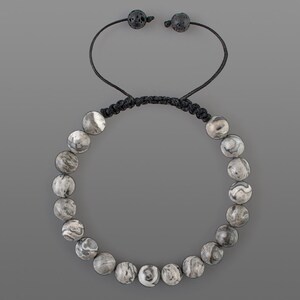 May include: A gray and white patterned stone beaded bracelet with black cord and adjustable closure.