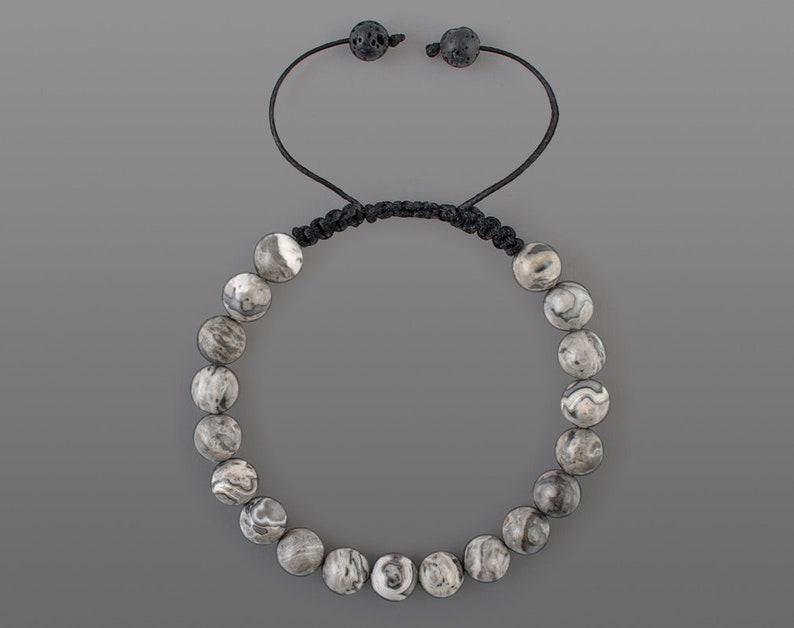 May include: A gray and white patterned stone beaded bracelet with black cord and adjustable closure.