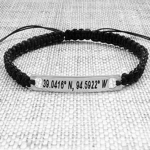 May include: Black braided bracelet with a silver tag engraved with the coordinates "39.0416&deg; N, 94.5922&deg; W".
