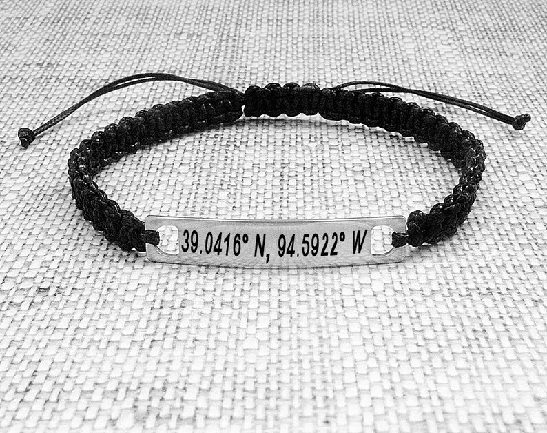 May include: Black braided bracelet with a silver tag engraved with the coordinates "39.0416&deg; N, 94.5922&deg; W".