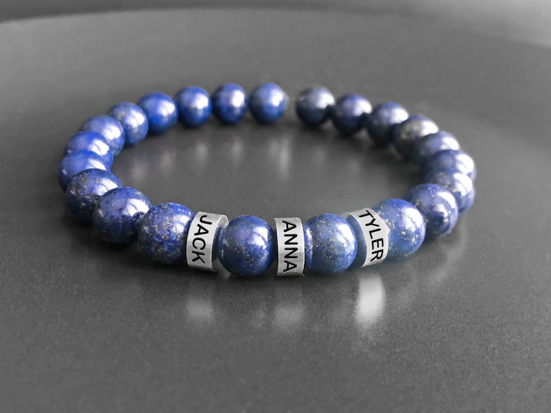 May include: A blue lapis lazuli beaded bracelet with silver beads engraved with the names "JACK", "ANNA", and "TYLER".