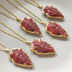 May include: Five gold necklaces with red and white arrowhead pendants. The arrowheads are made of natural stone and have a gold-plated edge.