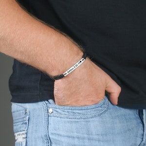 May include: A black braided bracelet with a silver bar that says "Ashton 2-26-19" with a small heart symbol.