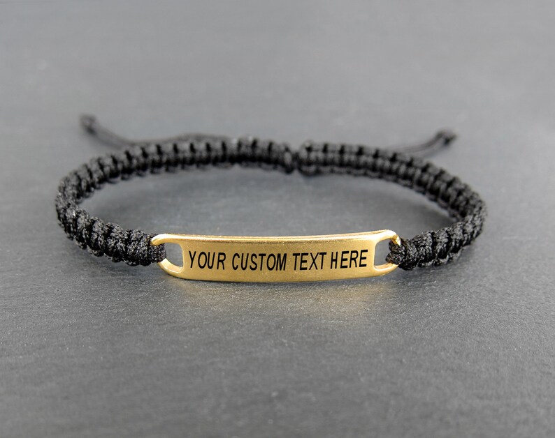 May include: A black braided bracelet with a gold metal tag that says "YOUR CUSTOM TEXT HERE".