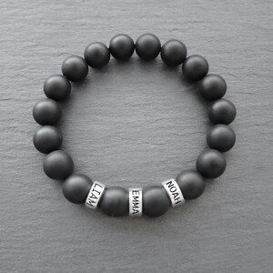 May include: Black beaded bracelet with silver beads that spell out the names "Liam", "Emma", and "Noah".