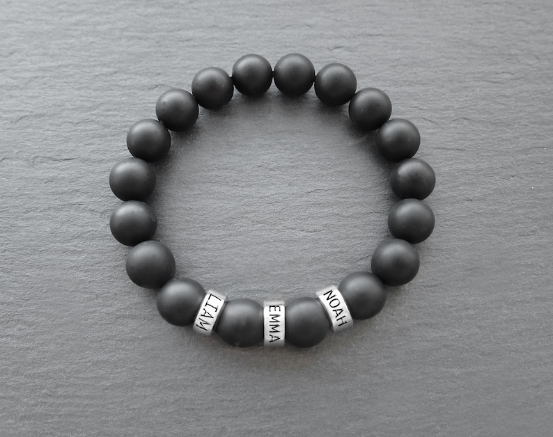 May include: Black beaded bracelet with silver beads that spell out the names "Liam", "Emma", and "Noah".