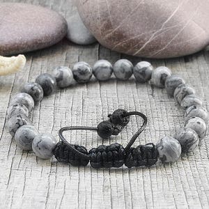 May include: Gray and black beaded bracelet with a black cord closure. The beads are made of a marbled stone.