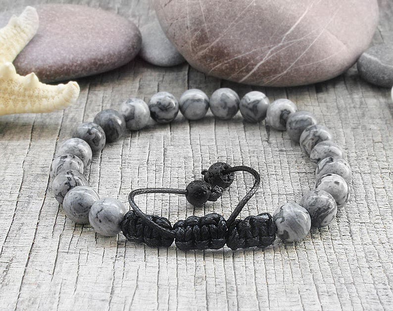 May include: Gray and black beaded bracelet with a black cord closure. The beads are made of a marbled stone.