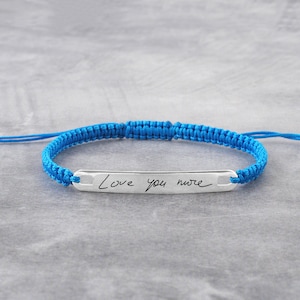 May include: A blue braided bracelet with a silver bar charm engraved with the handwritten message "Love you more".