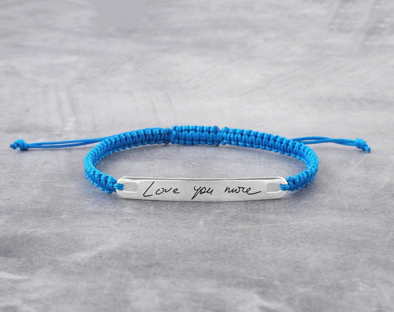 May include: A blue braided bracelet with a silver bar charm engraved with the handwritten message "Love you more".