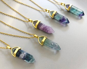 May include: Five gold necklaces with different colored fluorite crystal point pendants. The crystals are all different shades of purple, blue, and green.
