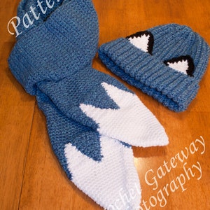 May include: A blue and white crocheted scarf and hat set with a white and black eye design on the hat. The set is laid out on a wooden surface. The text "Crochet Gateway Photography" is visible in the lower right corner of the image.