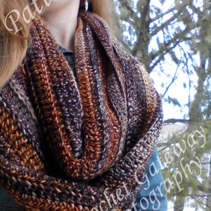 May include: A brown, orange and grey infinity scarf with a crocheted texture. The scarf is worn by a person with long blonde hair. The text "Crochet Gateway Photography" is visible in the lower right corner of the image.